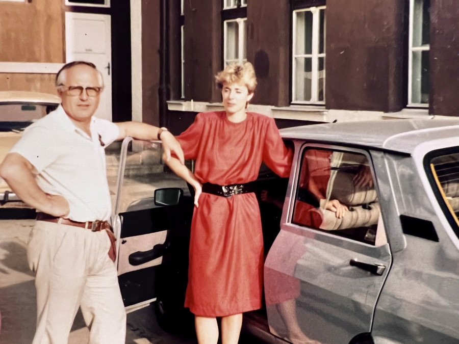 Archival family photo: Gabriel's mother in a red dress beside a car