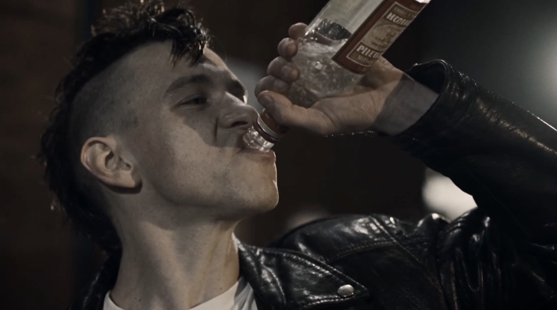 A mohawked skinhead drinking from a bottle
