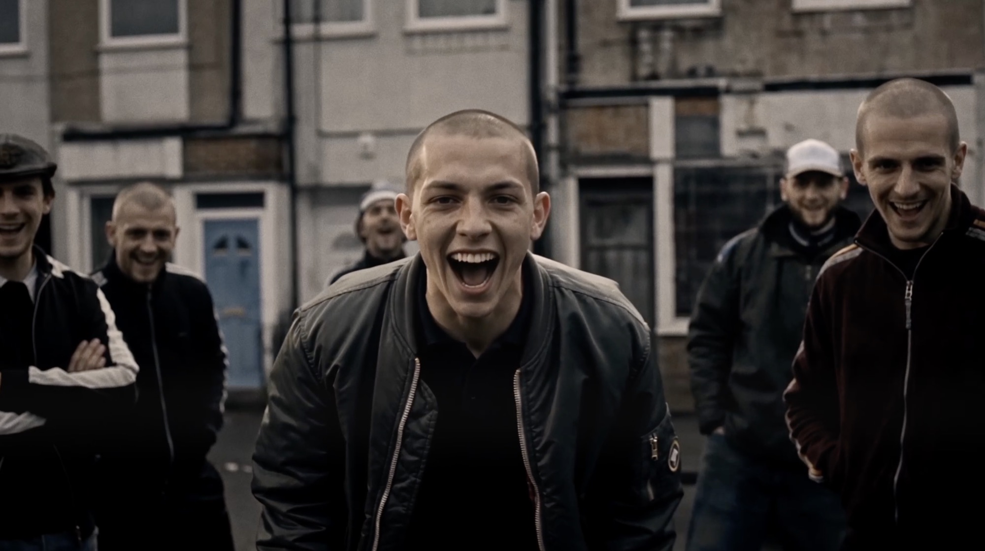 A grinning skinhead in a bomber jacket on a grey street