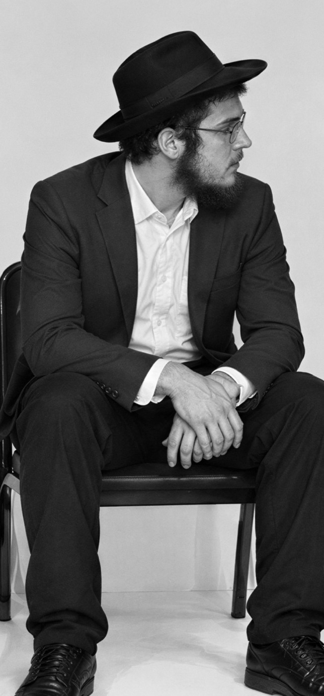 Gabriel as a Hasidic man, seated, looking over his shoulder
